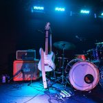 Electric guitar and drum set on an illuminated live music stage, ready for performance.